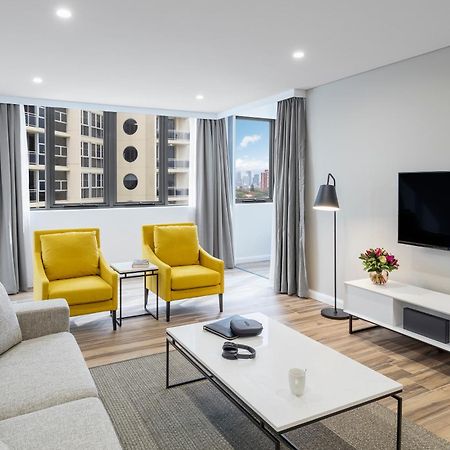 فندق أجنحة ميريتون بوندي جنكشن سيدني المظهر الخارجي الصورة The photo shows a modern, well-lit living room. It features a light gray sofa with a textured fabric. There are two bright yellow armchairs positioned near a window, which allows natural light to enter the space. The room has light gray curtains and 