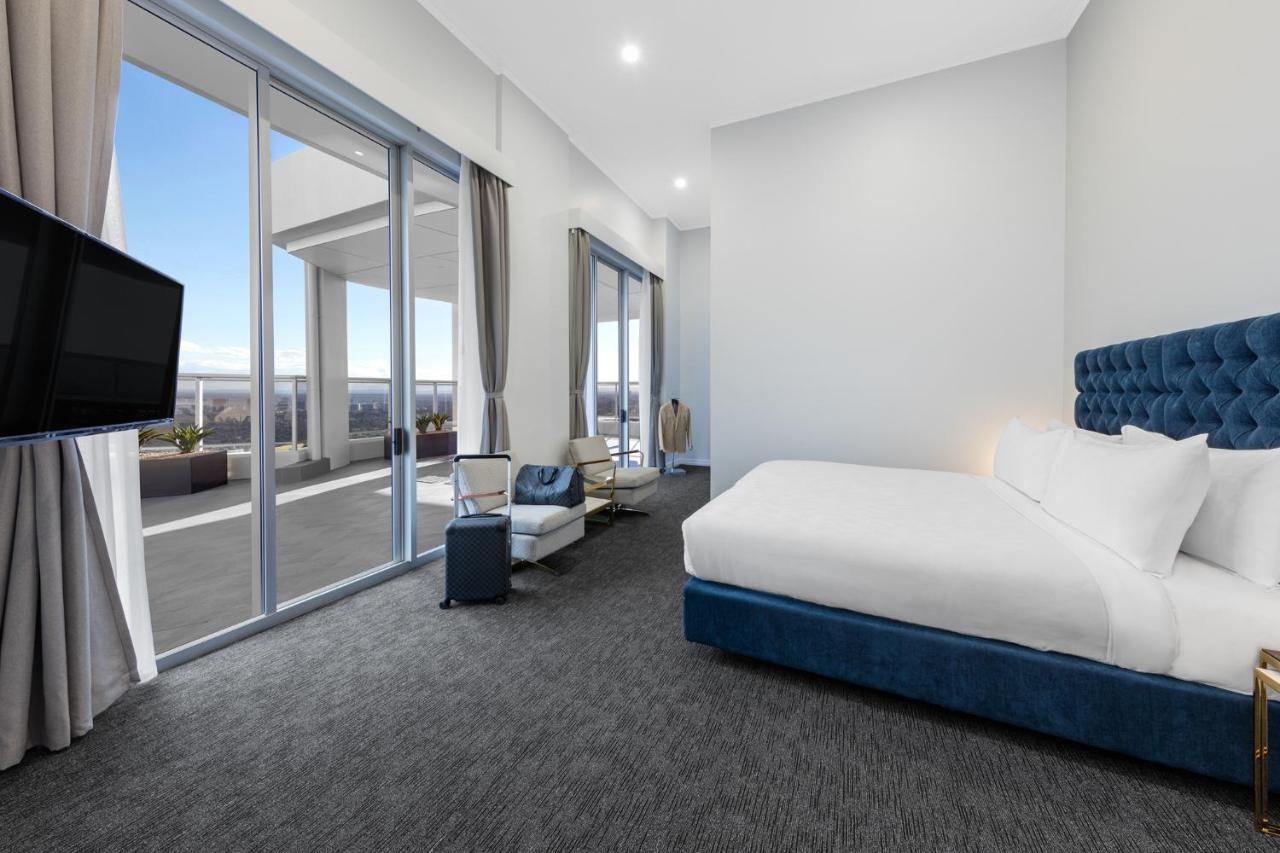 فندق أجنحة ميريتون بوندي جنكشن سيدني المظهر الخارجي الصورة The photo shows a modern and spacious hotel room. It features a large bed with a blue headboard, a flat-screen TV mounted on the wall, and a cozy seating area with a chair and small table. The room has large windows that offer natural light and a vie