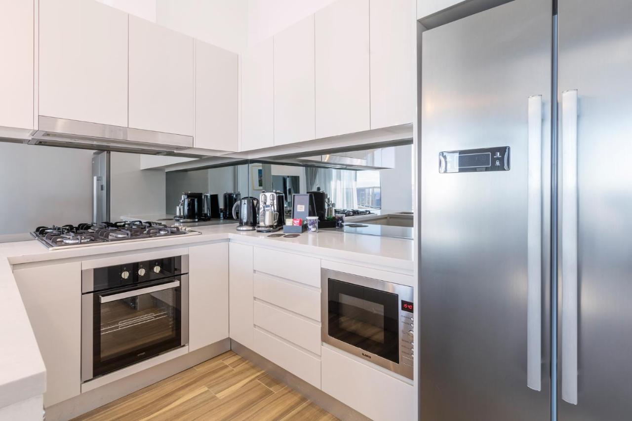 فندق أجنحة ميريتون بوندي جنكشن سيدني المظهر الخارجي الصورة The photo shows a modern kitchen with a clean and minimalist design. It features white cabinetry and a stainless steel refrigerator. The kitchen includes a gas stove with an oven below it, as well as a microwave. There are several kitchen appliances,