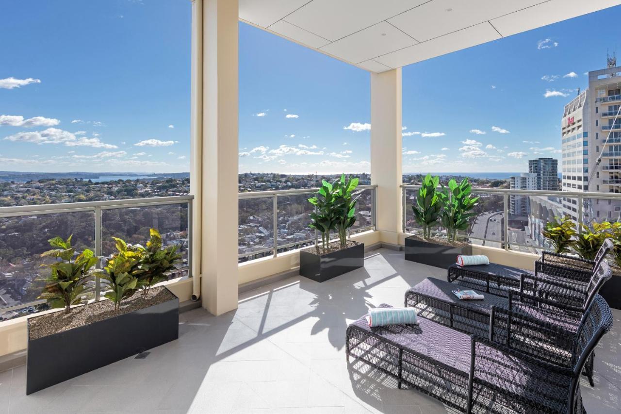 فندق أجنحة ميريتون بوندي جنكشن سيدني المظهر الخارجي الصورة The photo shows a modern balcony or terrace area with a stunning view. There are several planters with green plants placed along the edge. The seating area features lounge chairs in a contemporary design, likely made of woven materials. The space app