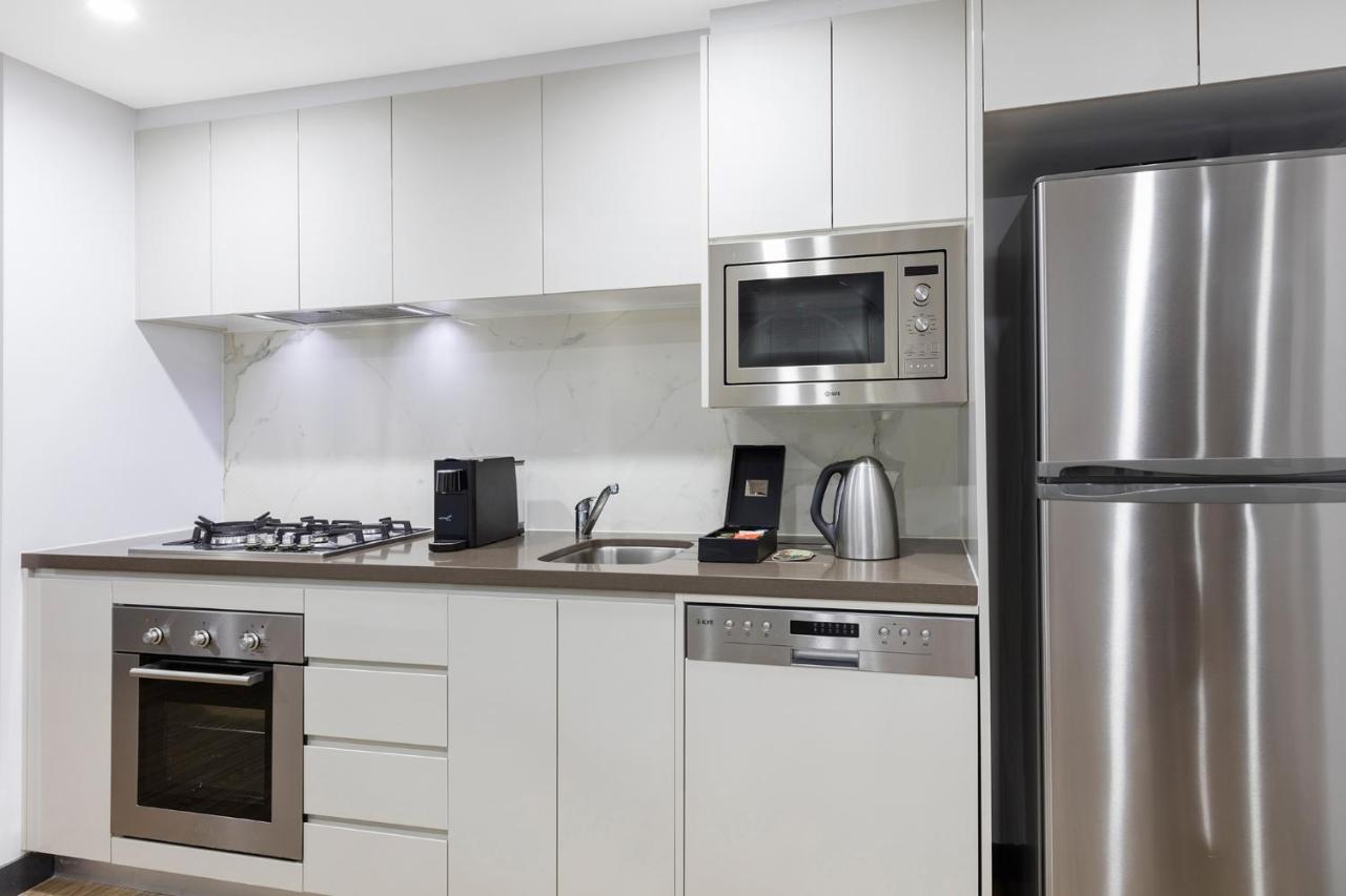 فندق أجنحة ميريتون بوندي جنكشن سيدني المظهر الخارجي الصورة The photo shows a modern kitchen with a sleek, minimalist design. It features white cabinetry and a countertop that blends with the overall aesthetic. 

Key elements include:

- A stainless steel refrigerator on the right.
- An oven with a gas cookto