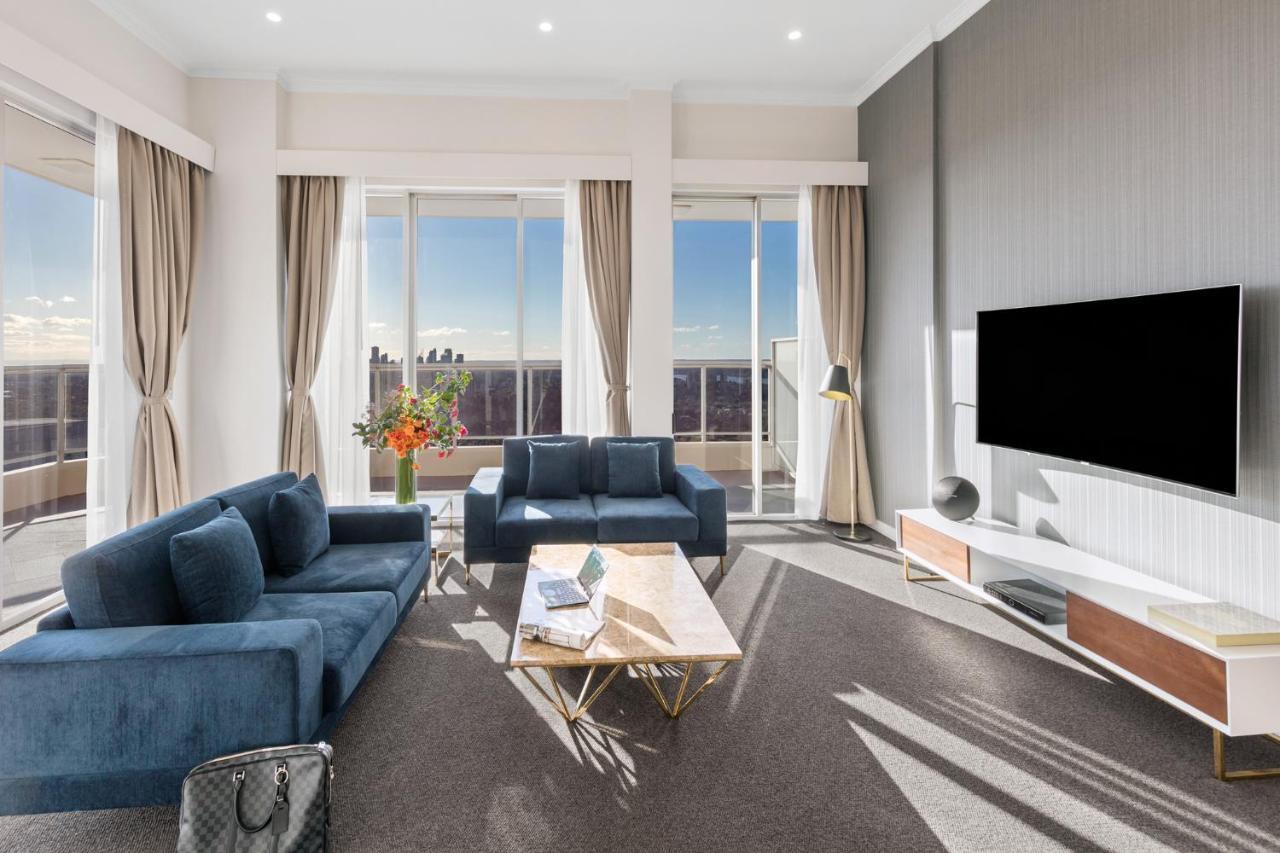 فندق أجنحة ميريتون بوندي جنكشن سيدني المظهر الخارجي الصورة The photo depicts a modern living room with a stylish and contemporary design. It features a cozy seating arrangement with a blue sofa and two matching armchairs. In front of the seating area is a coffee table with a geometric design. The room has la