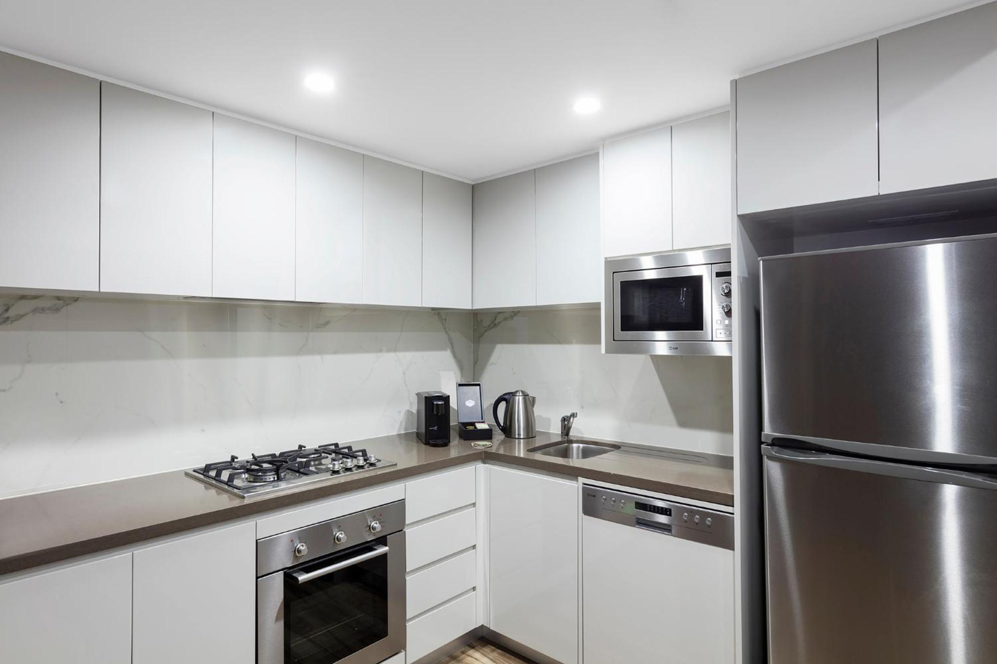 فندق أجنحة ميريتون بوندي جنكشن سيدني المظهر الخارجي الصورة The photo shows a modern kitchen featuring a minimalist design. It has light-colored cabinetry, a countertop, and stainless steel appliances. The appliances include a gas stove with multiple burners, an oven, a microwave, a kettle, and a refrigerator